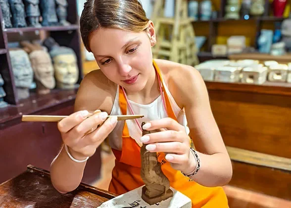 A traveller painting a small ceramic object in a workshop