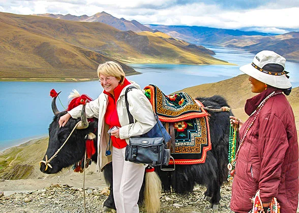 A traveller beside a decorated yak overlooking a mountain lake